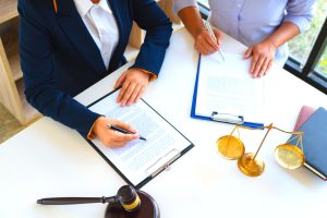 hands of attorneys, seated at a table with hands on documents as they negotiate; a gavel and justice scales are on the table